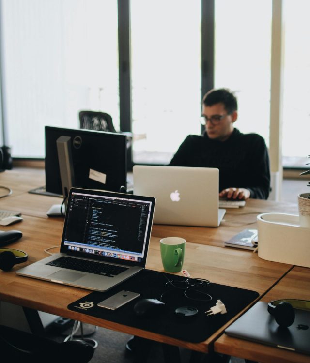 A web developer working on code in a modern office setting with multiple devices.